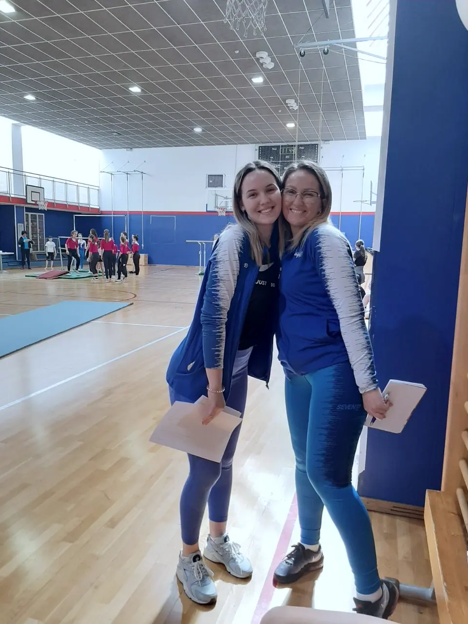 Dve trenerice u plavim klupskim jaknama zagrljene u sportskoj hali na takmičenju